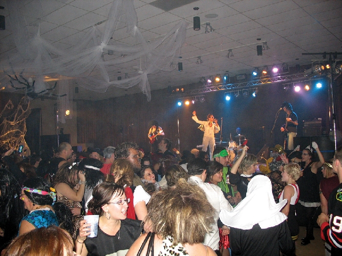 Dance floor full of people with a band on stage from previous years.