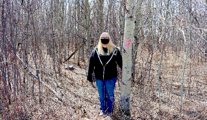 Assistant Rec Director Kelly Woywada poses at the first tree that will be removed to kick off the outdoor walking trail project.